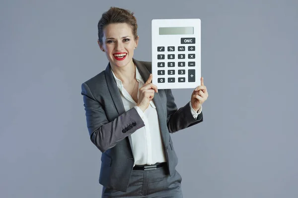 快乐时尚40岁的小企业主女人穿着灰色西服 带着灰色背景的计算器 — 图库照片