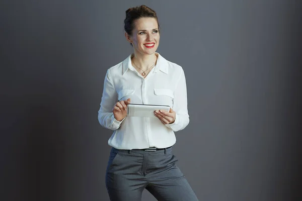 基于灰色背景的平板电脑应用的中年妇女白衬衫微笑小业主 — 图库照片