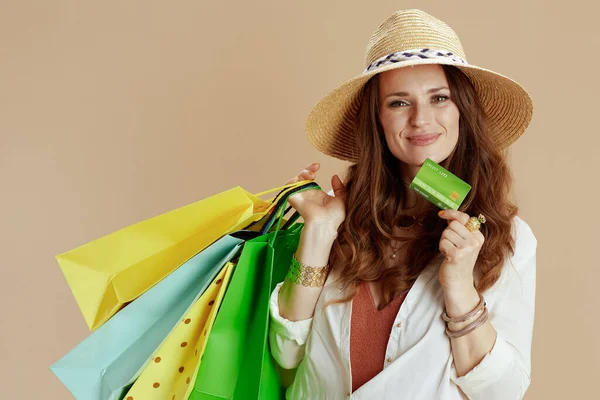 ビーチ休暇 幸せなエレガントな女性で白いブラウスとショートパンツ隔離でベージュの背景でクレジットカード ショッピングバッグと夏の帽子 — ストック写真