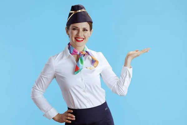 Uśmiechnięta Nowoczesna Stewardessa Niebieskim Tle Mundurze Prezentująca Coś Pustej Dłoni — Zdjęcie stockowe