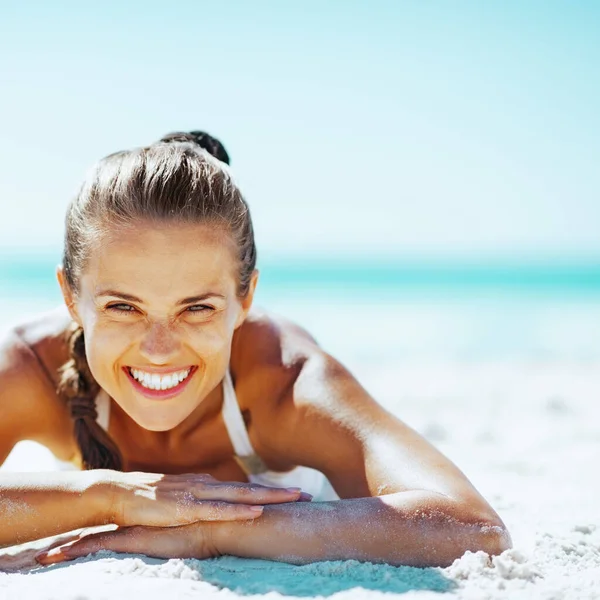 微笑的年轻女子在泳装躺在沙滩上 — 图库照片