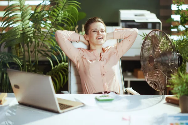 持続可能な職場 幸せな現代的な中年のブックキーパー女性と仕事で電動ファンとラップトップ — ストック写真