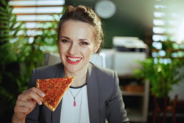 持続可能な職場 現代のグリーンオフィスでピザとグレーのビジネススーツを着た現代の女性従業員を笑顔 — ストック写真
