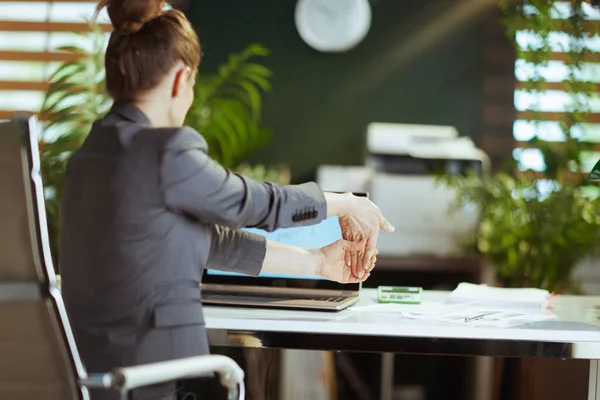 持続可能な職場 現代の緑のオフィスストレッチ手でグレーのビジネススーツで現代のビジネス女性の後ろから見た — ストック写真