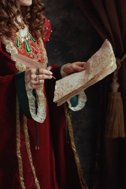 Kırmızı elbiseli ortaçağ kraliçesine yakın plan koyu gri arkaplanda parşömen var..