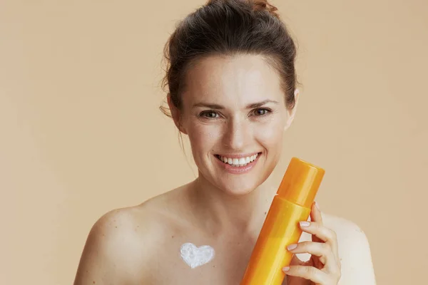 面带微笑的现代女人 胸前挂着化妆品奶瓶和心形奶油瓶 与米色隔离 — 图库照片