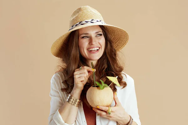 海滩度假 穿着白色衬衫和短裤的现代家庭主妇笑着 带着椰子鸡尾酒和夏帽 与米色背景隔离 — 图库照片