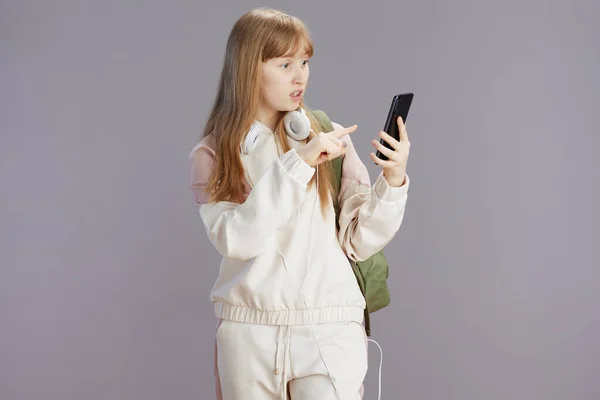 베이지 헤드폰을 소녀가 배경에서 고립된 스마트폰을 사용하는 놀라움을 못했다 — 스톡 사진
