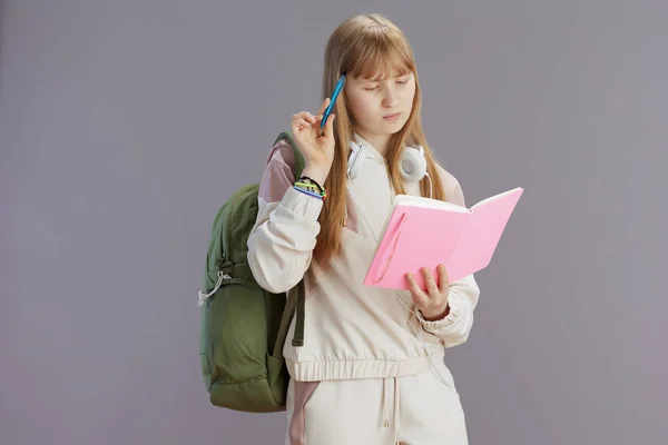 流行の10代の女の子でベージュのトラックスーツでバックパック ワークブック ヘッドフォンとペンはグレーの背景に隔離 — ストック写真