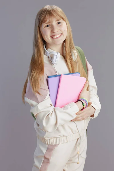 笑顔現代女子高生の肖像画でベージュトラックスーツとともにワークブックとヘッドフォン孤立した上灰色の背景 — ストック写真