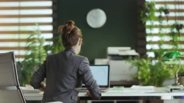 Sürdürülebilir iş yeri. İş yerinde bacaklarını esneten gri takım elbiseli modern iş kadınının arkasından görüldü..