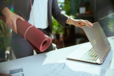 Sürdürülebilir iş yeri. Bilgisayarlı ve yoga minderli modern iş kadınına yakın çekim..