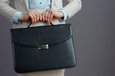 Gri arka planda evrak çantasıyla hafif bir iş elbisesi giymiş kadın işçiye yakın çekim..