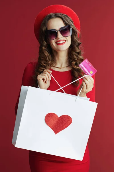 ハッピーバレンタイン 幸せなエレガントな40歳の女性で赤いドレスとベレー帽に赤い背景にクレジットカードとショッピングバッグとハート — ストック写真