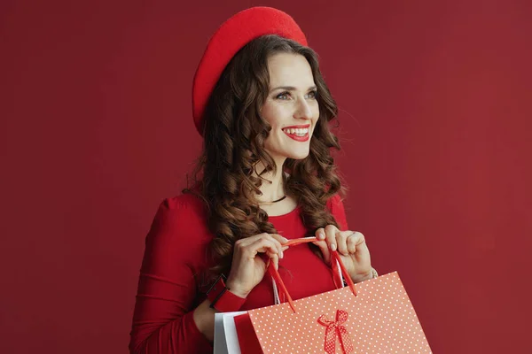 ハッピーバレンタイン 幸せなエレガントな女性とともに長い波状の髪で赤いドレスとベレー帽に赤い背景でショッピングバッグ — ストック写真