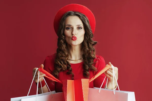 ハッピーバレンタイン エレガントな女性とともに長い波状の髪で赤いドレスとベレー帽上の赤い背景にショッピングバッグ送信Aキス — ストック写真
