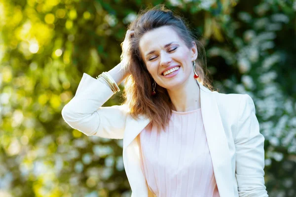 Sorrindo Elegante Fêmea Vestido Rosa Jaqueta Branca Cidade Contra Vegetação — Fotografia de Stock