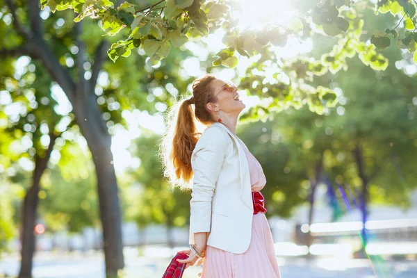 城市里快乐的中年妇女 身穿粉色衣服和白色夹克 戴着太阳镜 — 图库照片