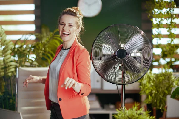 持続可能な職場 現代の40歳の女性労働者を笑顔現代の緑のオフィスで赤のジャケットに電動ファンダンス — ストック写真