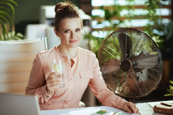 持続可能な職場 現代のグリーンオフィスで働く女性の笑顔を電気ファン水とレモンで — ストック写真