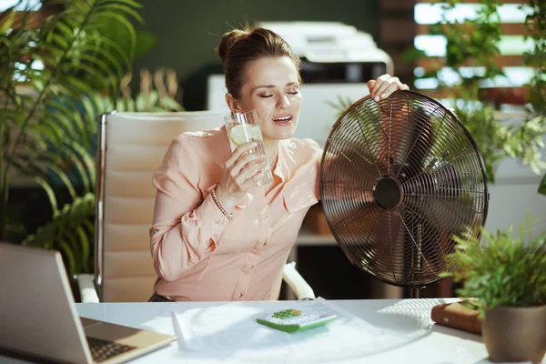 持続可能な職場 現代のグリーンオフィスで働く女性の笑顔を電気ファン水とレモンで — ストック写真