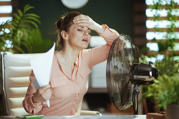 持続可能な職場 現代の40歳の女性従業員夏の暑さに苦しむ書類やファンと仕事をしています — ストック写真