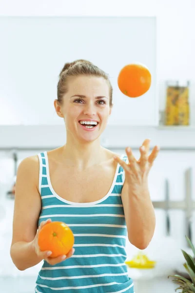 キッチンでオレンジとジョグリング幸せな若い女 — ストック写真