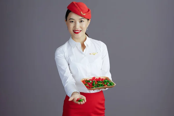 Uśmiechnięta Stylowa Azjatycka Stewardessa Czerwonej Spódnicy Kapeluszu Mundur Cukierkami Szarym — Zdjęcie stockowe