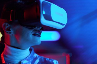 Neon metaevren fütüristik konsepti. Siyah arka planda VR kulaklıklı orta yaşlı trend kadın portresi.