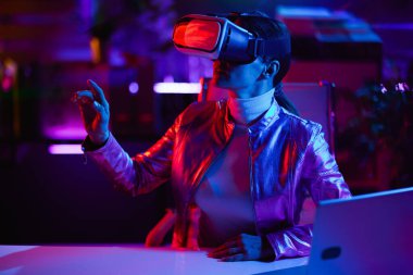Neon metaevren fütüristik konsepti. VR kulaklıklı şık iş kadını modern ofiste sanal gerçeklik tasarlıyor..