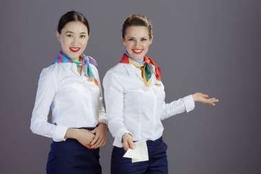 Mavi etekli, beyaz gömlekli ve eşarplı zarif bayan uçuş görevlileri gri üzerine ayrılmış uçak biletleriyle.