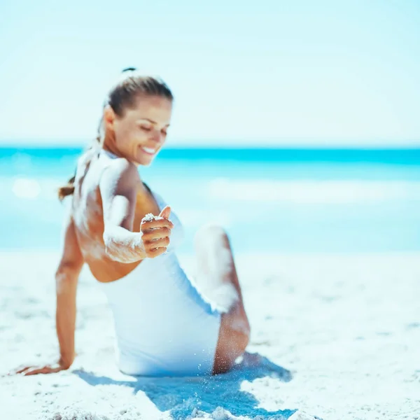 水着ビーチに座っていると砂で遊ぶ笑顔若い女性へのクローズ アップ — ストック写真