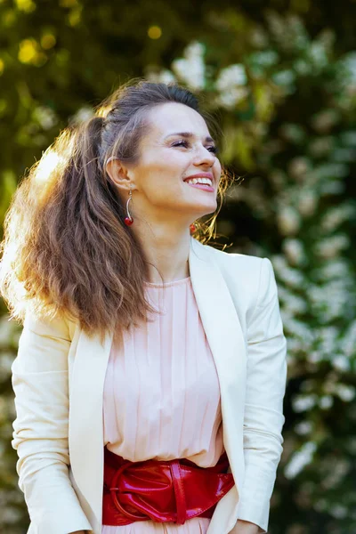 Glimlachende Elegante Vrouw Roze Jurk Witte Jas Stad Tegen Groen — Stockfoto