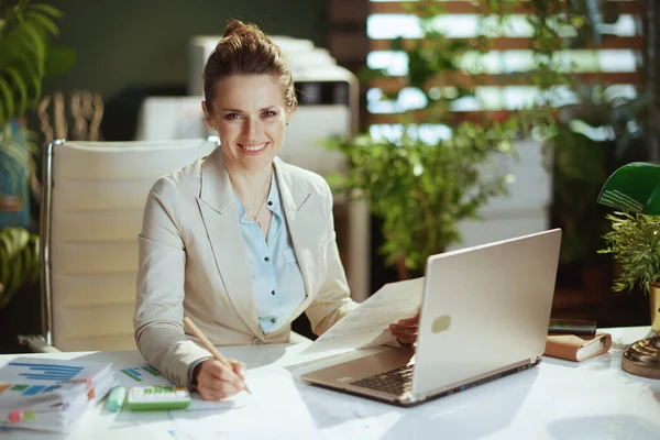 文書やノートパソコンと現代の緑のオフィスで軽いビジネススーツの幸せな現代会計士の女性の肖像 — ストック写真