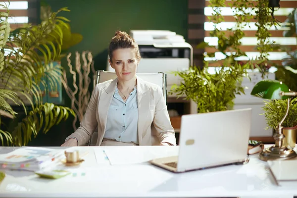 現代的な中年中小企業の所有者の肖像ノートパソコンと現代の緑のオフィスで軽いビジネススーツの女性 — ストック写真