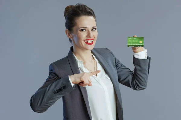 幸せな中年小ビジネス所有者女性でグレースーツとともにクレジットカードでグレー背景 — ストック写真