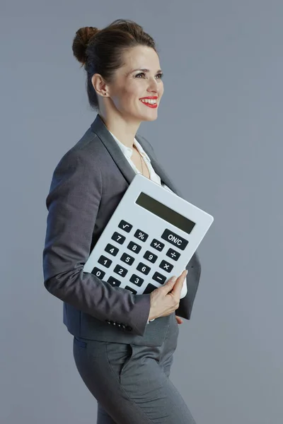 40岁快乐的女商人 穿着灰色西装 带着灰色背景的计算器 — 图库照片