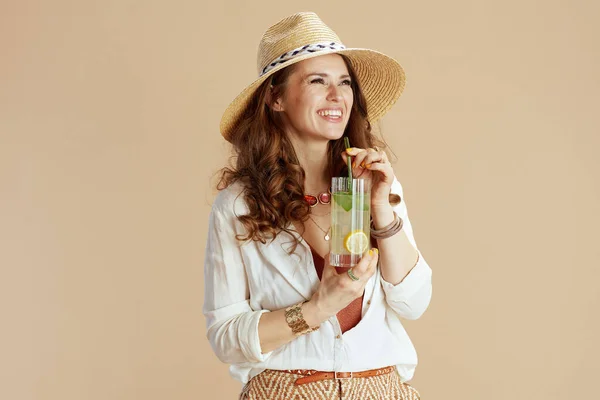 海滩度假 穿着白衬衫 穿着米色背景短裤 戴着鸡尾酒和夏帽的现代女性微笑 — 图库照片