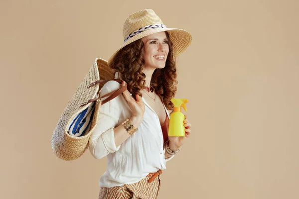 ビーチ休暇 幸せなスタイリッシュな主婦で白いブラウスとショートパンツ隔離されたベージュでストローバッグ 日焼け止めと夏の帽子 — ストック写真