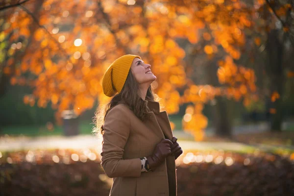 10月份 城市公园里穿着米黄色外套 头戴橙色帽子 面带微笑的女性 — 图库照片