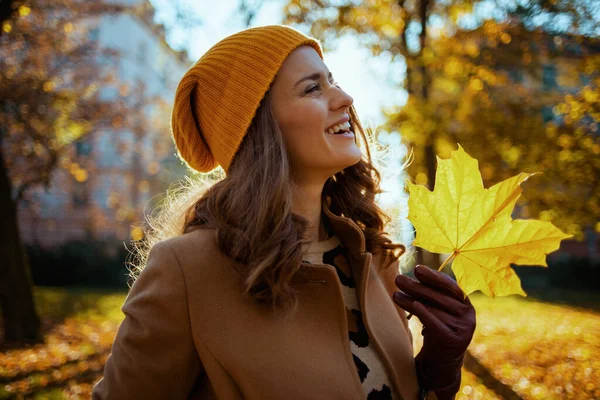 十一月 今年秋天 城市里身穿米黄色外套 头戴橙色帽子 头戴秋天黄色叶子的40岁的老妇面带微笑 — 图库照片