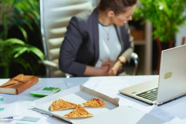 Sürdürülebilir iş yeri. Yeşil ofisteki gri takım elbiseli, pizza ve dizüstü bilgisayarı olan orta yaşlı muhasebeci kadına yakın çekim..