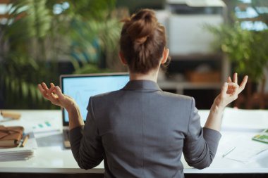 Sürdürülebilir iş yeri. İş yerinde meditasyon yapan gri takım elbiseli, modern, küçük işletme sahibi bir kadının arkasından görüldü..