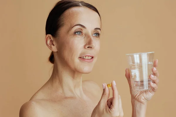 modern 40 years old woman with glass of water and pill isolated on beige.