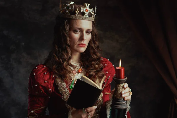 穿着红色衣服 头戴深灰色背景的书籍 蜡烛和王冠的中世纪沉思女王 — 图库照片