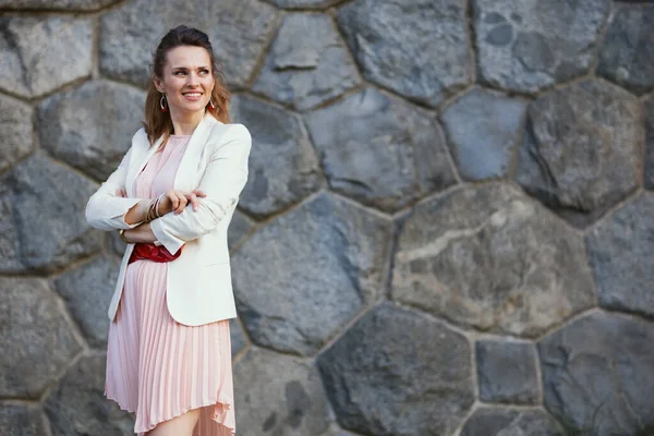 幸せな若い女性ピンクのドレスと白いジャケット市内の石の壁に対して — ストック写真