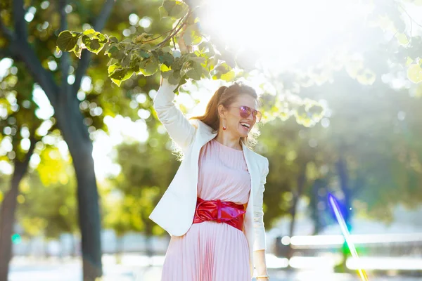 城市里快乐的现代女性 身穿粉色衣服 身穿白色夹克 戴着太阳镜 — 图库照片