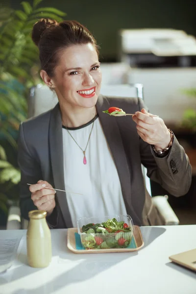 持続可能な職場 幸せな現代中年女性労働者で灰色のビジネススーツで現代緑のオフィス食べるサラダ — ストック写真