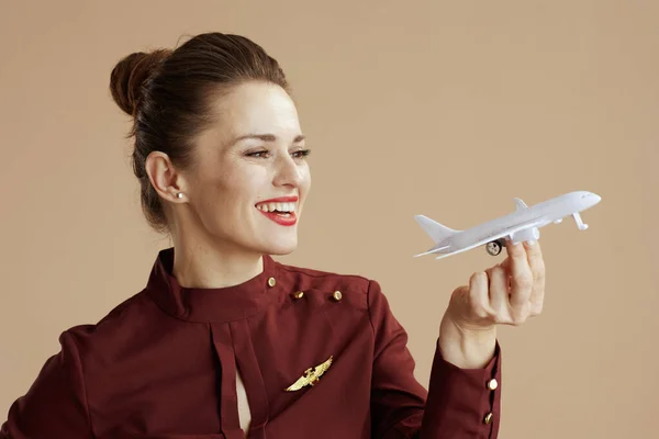 Leende Elegant Kvinnlig Flygvärdinna Mot Beige Bakgrund Med Lite Flygplan — Stockfoto