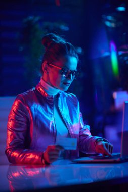 Neon metaverse futuristic concept. modern woman in glasses with laptop and credit card in modern office.